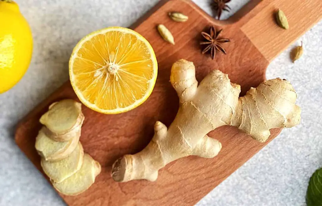 Pieces of cut ginger and a lemon on a wooden cutting board.