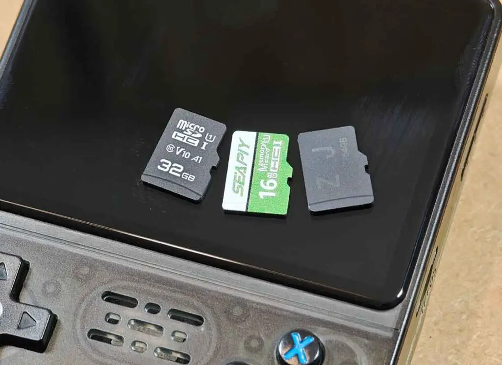 Three microSD cards placed on the R36S screen: a generic Qilive card on the left, a V90S stock card in the middle, and a stock R36S card on the right.